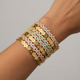 Gold bracelet with gemstones on a wrist against a gray background